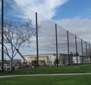 Tall, thin vertical panels installed in a line at a park near a commercial building, under a cloudy sky, used as golf netting.