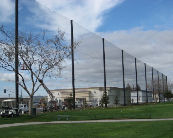 Tall, thin vertical panels installed in a line at a park near a commercial building, under a cloudy sky, used as golf netting.