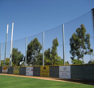 Baseball field with high Sports Netting and surrounding advertisements, accompanied by tall light poles and trees.