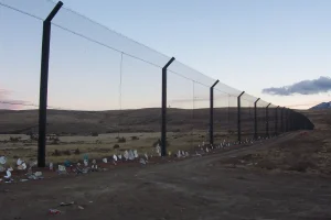 Tall border fence extending through the barren landscape of Bass Hill Landfill at dusk, with white bags lined up at the base.
