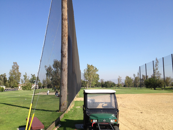 Judge Netting Barrier Specialists: A golf cart parked on a golf course surrounded by barrier and driving range netting.