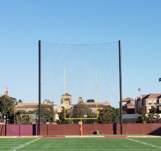 Football goalposts with netting on an empty field with a university building in the background on a clear day.