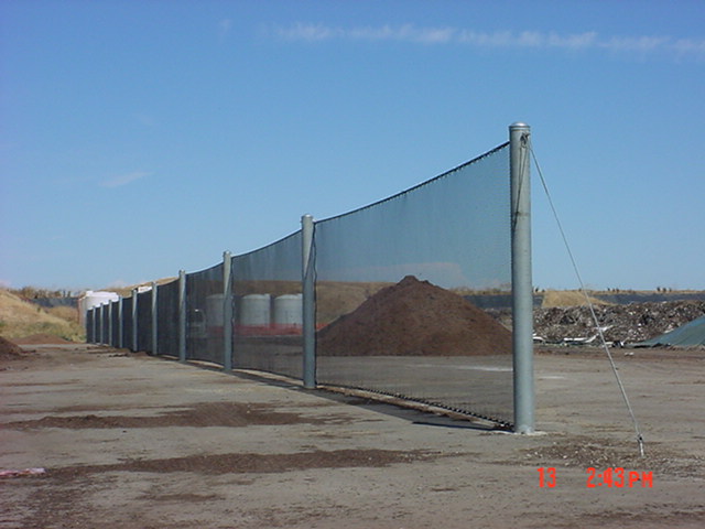 Judge Netting Barrier Specialists: A barrier fence with a pile of dirt next to it, acting as a boundary and litter containment for a landfill.