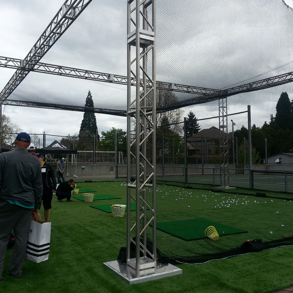 People practicing at an outdoor driving range with baskets of golf balls, sports netting, and artificial turf.