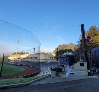 Golden hour sunlight bathes the University of Berkeley baseball field, highlighting the curve of safety netting and the surrounding stadium infrastructure.