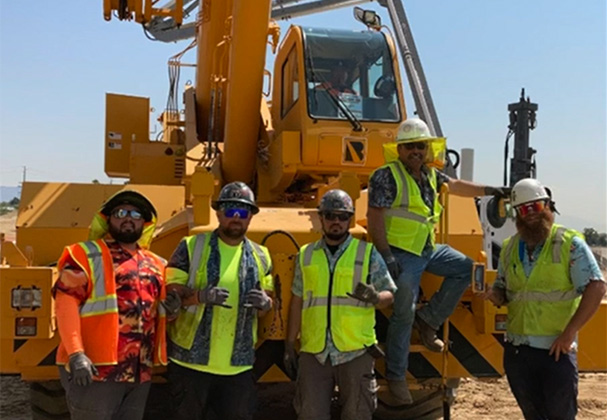Judge Netting Barrier Specialists: A group of construction workers in high-visibility vests, highlighting employment opportunities, posing in front of heavy machinery on a construction site.