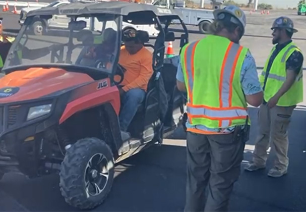 Judge Netting Barrier Specialists: Construction workers in safety vests discuss employment opportunities during an onsite meeting, with a utility vehicle in the foreground.