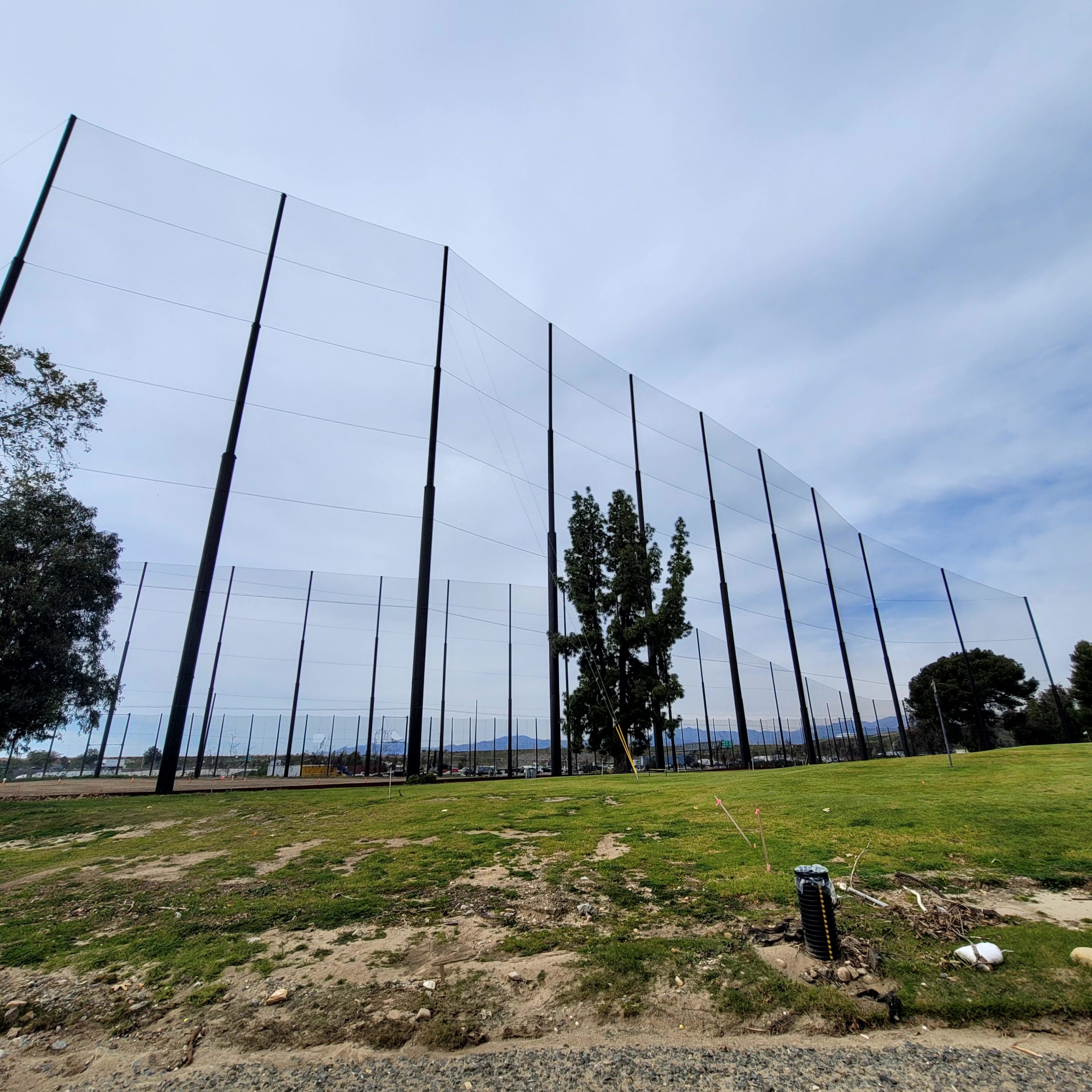 Tall fairway barriers surround an open grassy area with a few scattered trees under a cloudy sky at Diamond Bar Golf Course