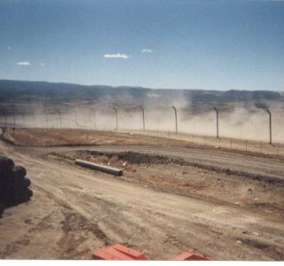 Judge Netting Barrier Specialists: A dirt road with a fence in the background, surrounded by landfill netting barriers.