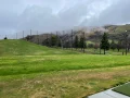 Overcast sky above the vibrant green fairway of Spring Valley Golf Course, with tall safety netting posts lined up along the slope.